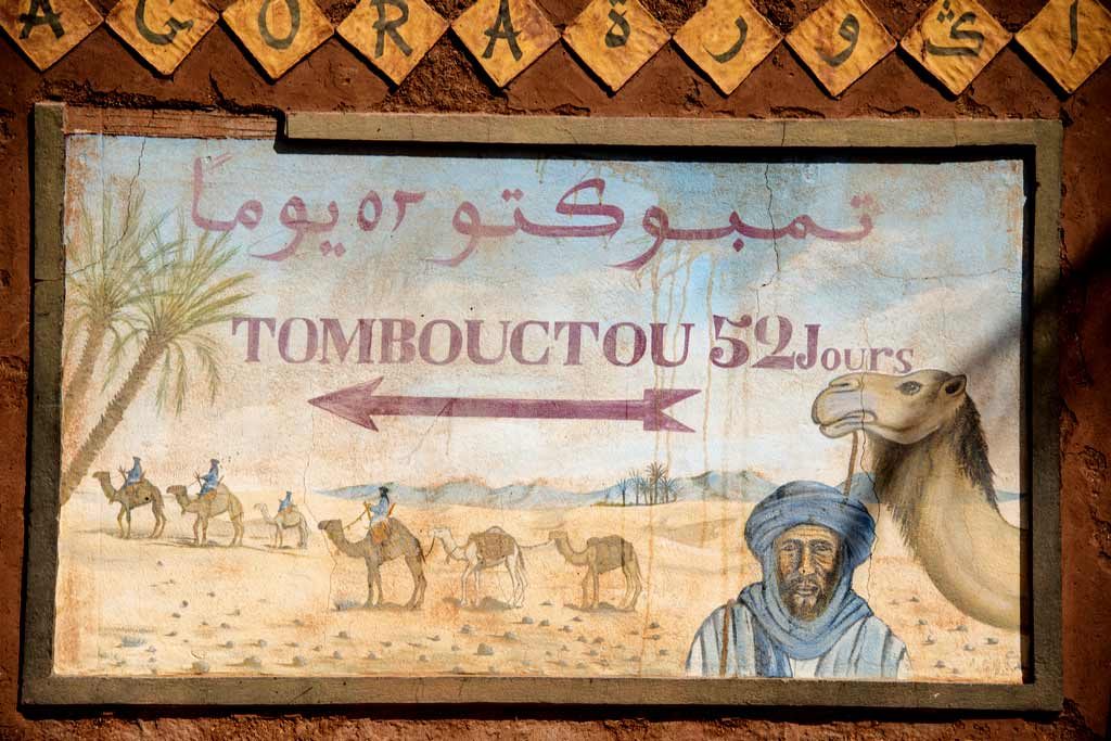 QUARZAZATE, MOROCCO, MARCH 8, 2014. A sign with a berber in the desert with a camel and an arrow pointing to Timbuktu, saying “52 days to Timbuktu” in Quarzazate, Morocco, on March 8th, 2014