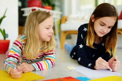 Two young sisters drawing with colorful pencils at home
