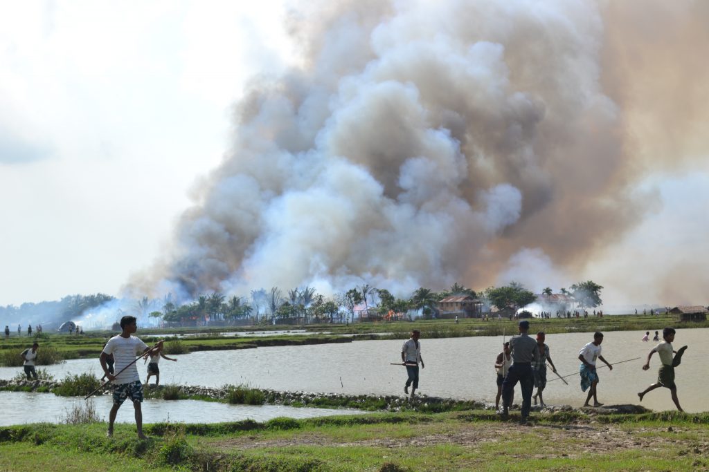 Ethnic Arakanese with weapons walking away from a village in flames while a soldier stands by. Arakan State, Burma, June 2012. © 2012 Human Rights Watch