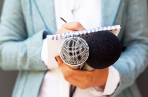 female-journalist-at-news-conference-writing-notes-holding-microphone-v