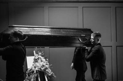 A group of men in formal attire carrying a wooden coffin-