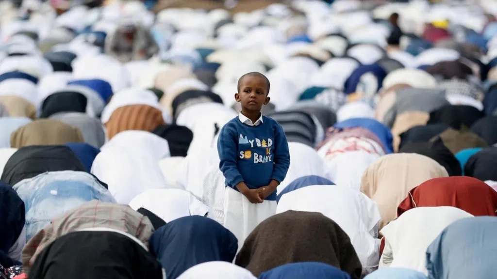 A boy stands in the middle of a crowd of people praying in Nairobi, Kenya.