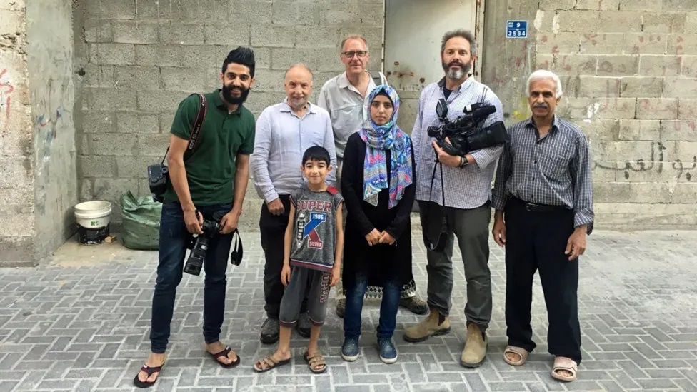 Asmaa, pictured with Paul Adams behind her, alongside the BBC team and her family outside their home