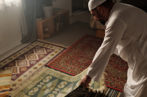 Muslim man laying prayer mat on floor