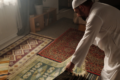 Muslim man laying prayer mat on floor