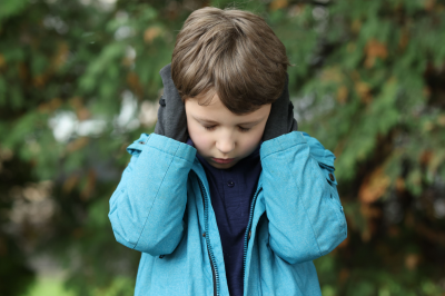 Autistic lonely Little Boy Covering His Ears Outdoors