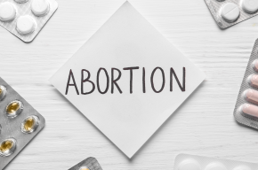 Paper note with word Abortion and pills on white wooden background, flat lay